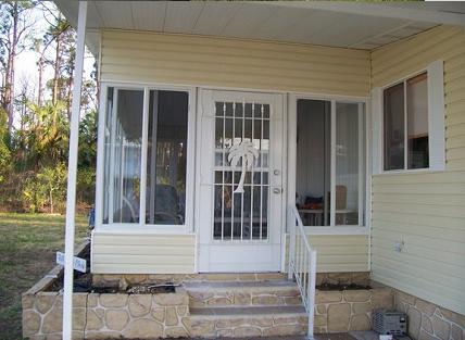 Screen room entry with a white aluminum screen door and vinyl windows on a Florida home