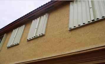 Storm protection installed on the upper windows of a stucco home